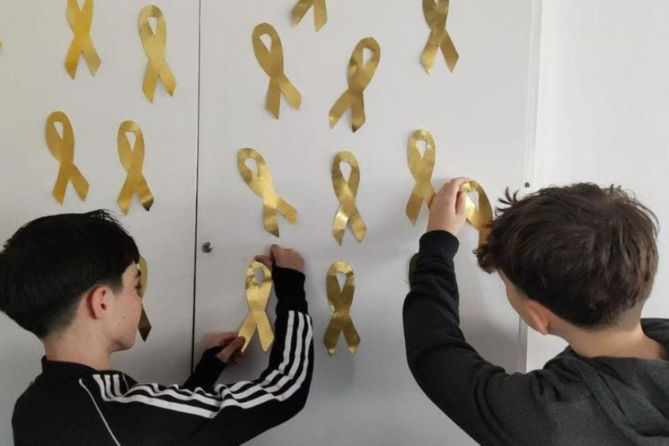 niños pegando lazos dorados en una pared blanca