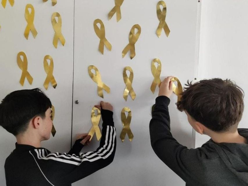 niños pegando lazos dorados en una pared blanca